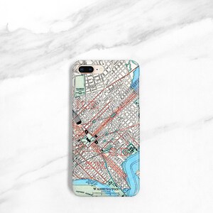 May include: A white iPhone case featuring a vintage map of Washington, D.C. printed on it. The map depicts the city's streets, parks, and waterways. The case has a gold trim around the edges.