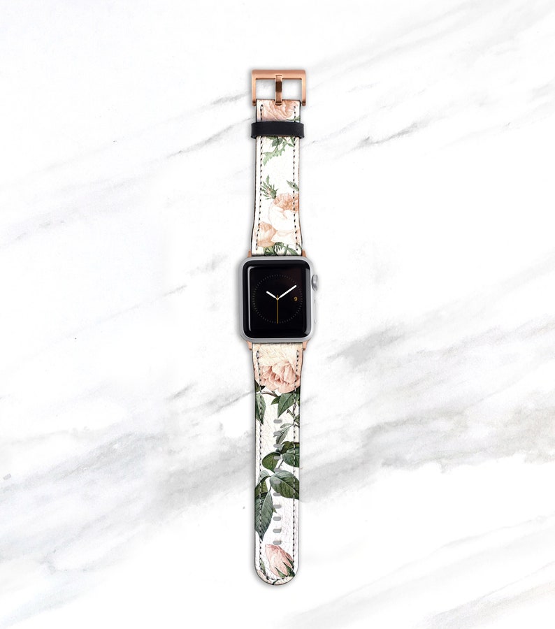 Op de afbeelding: Een witte Apple Watch met een band met bloemenprint. De band heeft een rozenpatroon met roze en groene accenten. De wijzerplaat van het horloge is zwart met witte wijzers en cijfers.