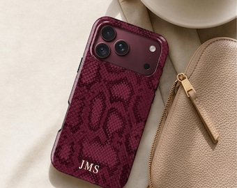May include: A deep burgundy smartphone case featuring a dark snakeskin pattern and the gold-colored initials JMS printed at the bottom. The case has a cutout for a triple-lens camera system and a flash, with a glossy finish throughout.