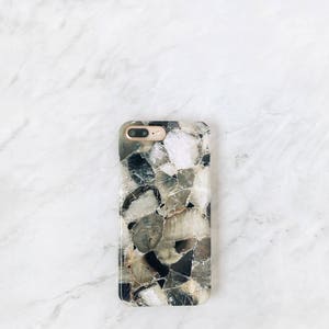 May include: A black and white phone case with a geometric pattern of different sized stones. The case has a gold camera lens.