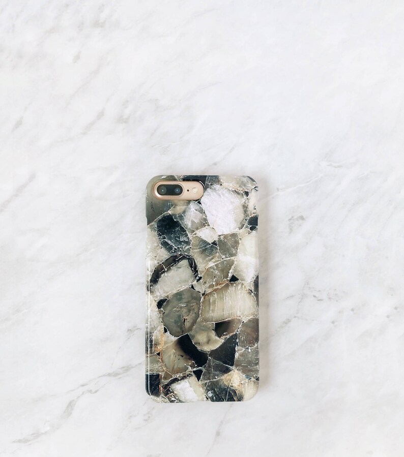 May include: A black and white phone case with a geometric pattern of different sized stones. The case has a gold camera lens.