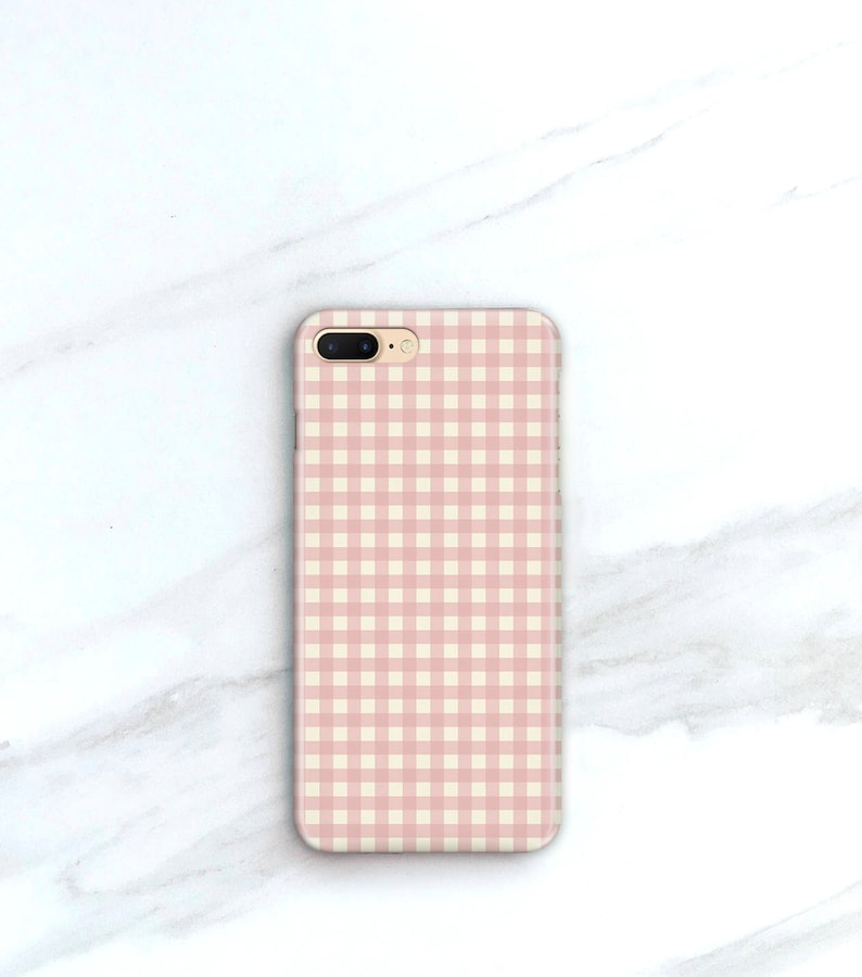Pu&ograve; includere: Custodia per telefono con motivo a quadri rosa e bianchi. La custodia rettangolare ha un'apertura per l'obiettivo della fotocamera. Lo sfondo &egrave; una superficie di marmo bianco.