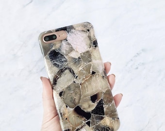 May include: A rectangular smartphone case featuring a mosaic pattern of polished, semi-translucent stone fragments in shades of beige, brown, black, and pale pink. The case has a smooth, glossy finish and a cutout for a dual-lens camera system.