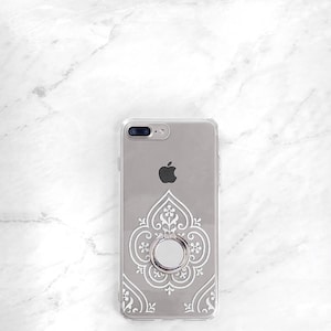 May include: A clear phone case with a white intricate design and a silver ring holder. The case is designed for an iPhone.