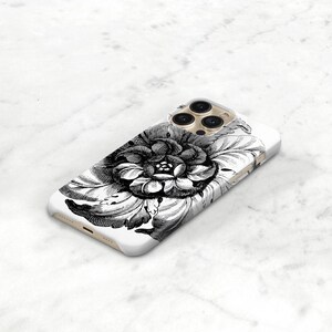 May include: White phone case featuring a detailed black and white floral design. The illustration depicts a large, open flower with intricate petal details. The case has a glossy finish and a camera bump.