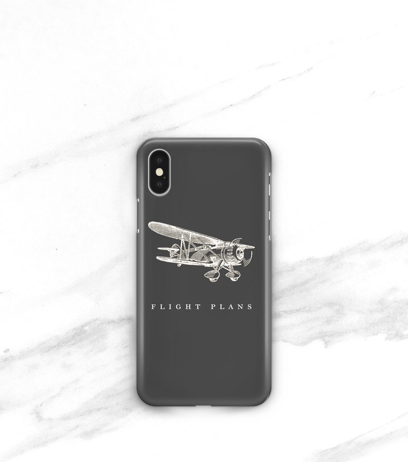 Peut inclure: Coque de t&eacute;l&eacute;phone gris fonc&eacute; avec une illustration d'avion vintage blanche. Les mots "FLIGHT PLANS" sont imprim&eacute;s en dessous. La coque est con&ccedil;ue pour un smartphone.