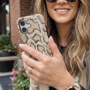 May include: A smartphone case featuring a textured brown and cream snakeskin pattern. The case has a cutout for a dual-lens camera system. The design covers the back and sides of the phone, providing a detailed reptilian scale aesthetic.