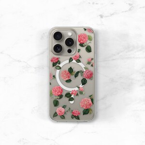May include: A clear phone case with a floral design featuring pink flowers and green leaves. The case has a white magnetic ring on the back.