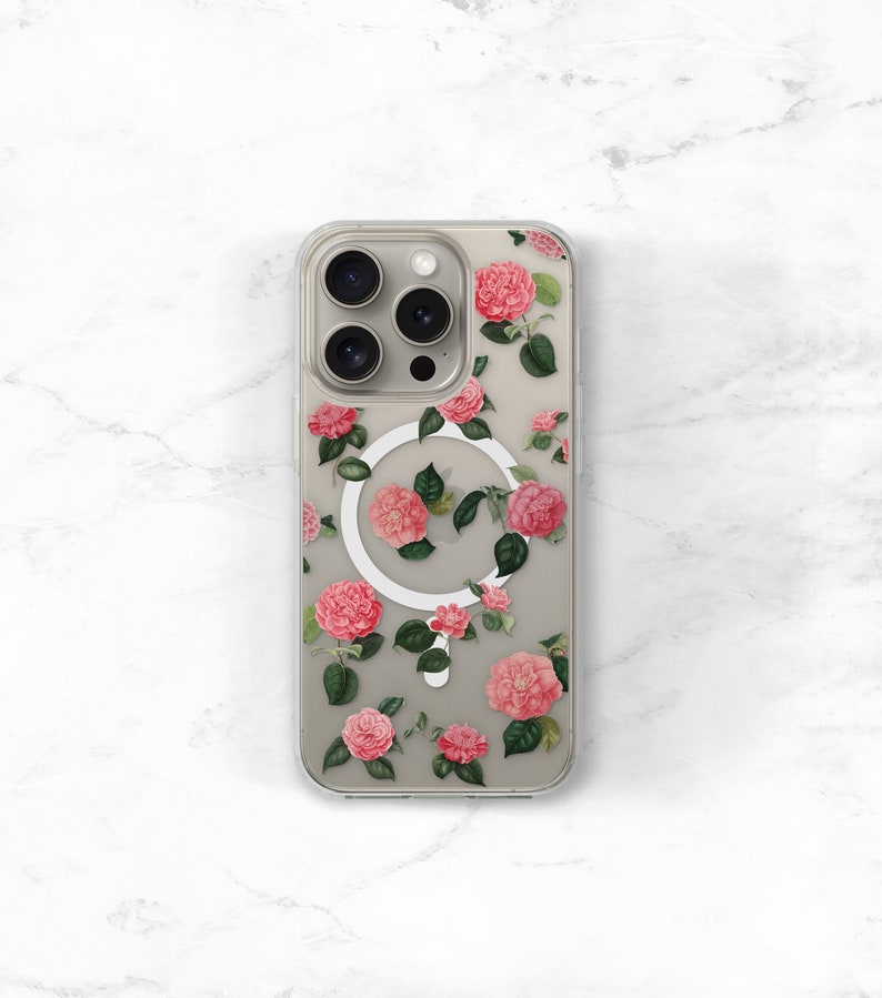 May include: A clear phone case with a floral design featuring pink flowers and green leaves. The case has a white magnetic ring on the back.
