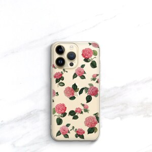 May include: A clear phone case with a floral design. The case features pink and white flowers with green leaves on a cream background.