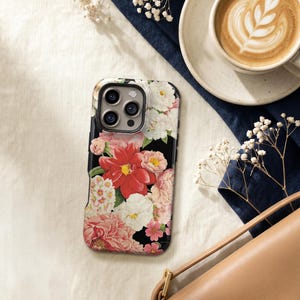 a floral phone case, a cup of coffee, a purse, and some flowers on a white surface.