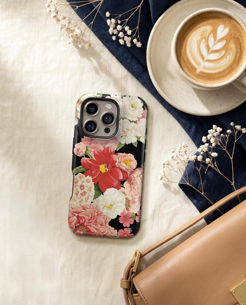 a floral phone case, a cup of coffee, a purse, and some flowers on a white surface.