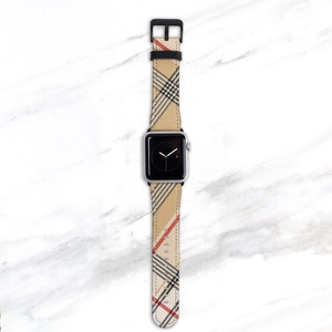 May include: A silver Apple Watch with a black and beige plaid patterned band. The band has red accents.