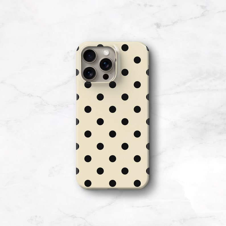Puede incluir: Una funda para tel&eacute;fono de color crema con un patr&oacute;n de lunares negros. La funda tiene un recorte para el objetivo de la c&aacute;mara del tel&eacute;fono.