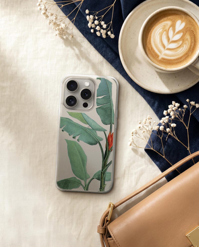 a smartphone with a plant-themed case, a cup of coffee, a purse, and some white flowers on a white surface.