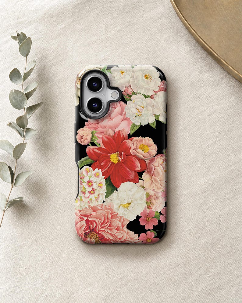 a phone case with a floral design, including red and pink flowers, placed on a beige surface.