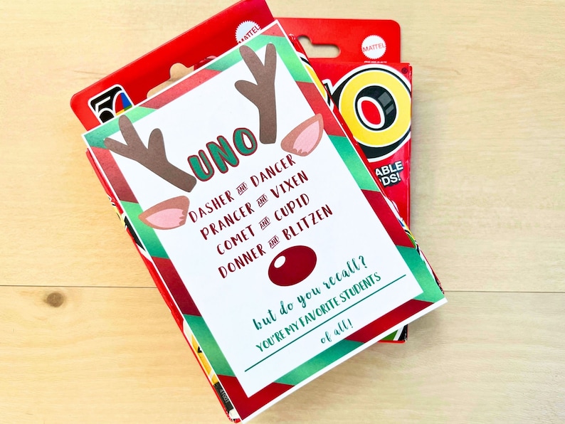 May include: A festive UNO card game box with a custom reindeer-themed design. The card features reindeer antlers, ears, and the names of Santa's reindeer. Text on the card reads "but do you recall? You're my favourite students of all!"