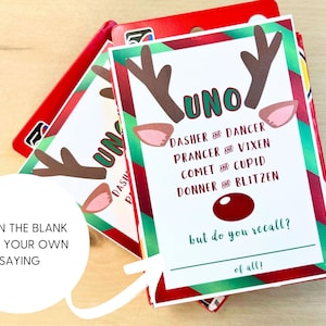 May include: A Christmas-themed Uno card game featuring reindeer antlers and ears. The cards display the word "UNO" and the names of Santa's reindeer. The text "Fill in the blank with your own saying" is also visible on the card.