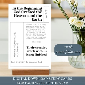 May include: A white study card with black text, including Bible verses and the text "In the Beginning God Created the Heaven and the Earth." The card is displayed on a wooden stand, with a vase of white flowers in the background.