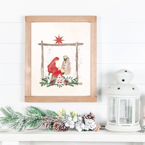 May include: A watercolor painting of the nativity scene with Mary, Joseph, and baby Jesus in a manger. The painting is framed in a light wood frame and is hanging on a white wall.