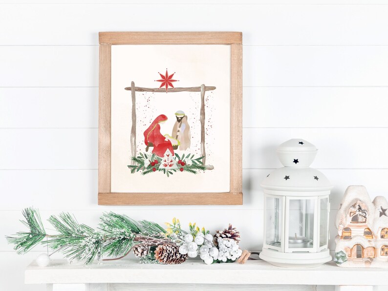 May include: A watercolor painting of the nativity scene with Mary, Joseph, and baby Jesus in a manger. The painting is framed in a light wood frame and is hanging on a white wall.