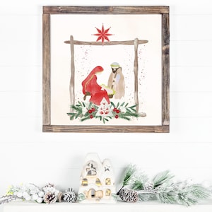 May include: A framed watercolor painting of the nativity scene with Mary, Joseph, and baby Jesus. The painting is set against a white background with a red star above the manger. The frame is brown wood.
