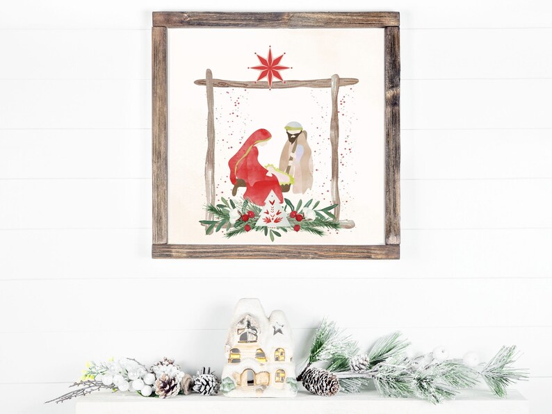 May include: A framed watercolor painting of the nativity scene with Mary, Joseph, and baby Jesus. The painting is set against a white background with a red star above the manger. The frame is brown wood.
