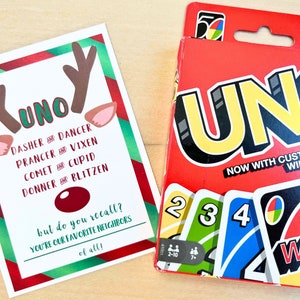 May include: A Christmas-themed card with reindeer antlers and ears, the word "UNO," and the names of Santa's reindeer. Beside it is a red UNO card game box with the word "UNO" in large yellow letters and a "WILD" card.
