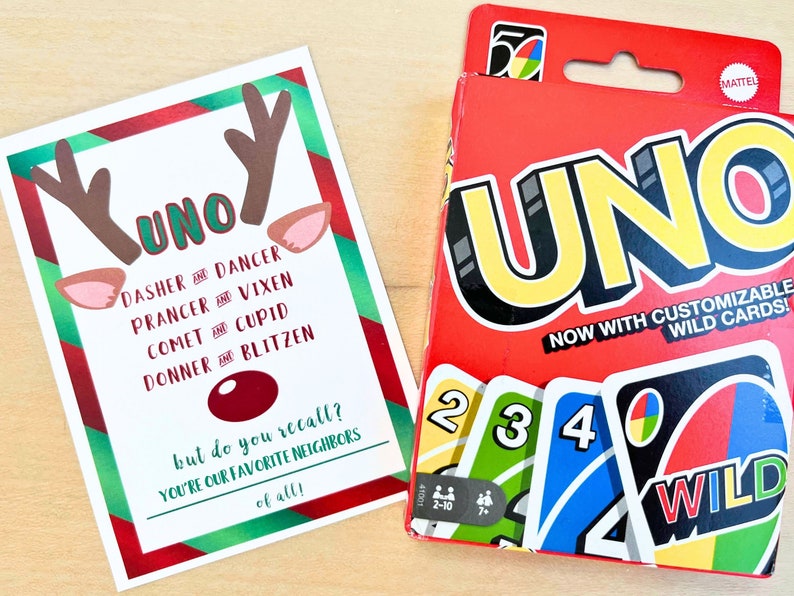 May include: A Christmas-themed card with reindeer antlers and ears, the word "UNO," and the names of Santa's reindeer. Beside it is a red UNO card game box with the word "UNO" in large yellow letters and a "WILD" card.