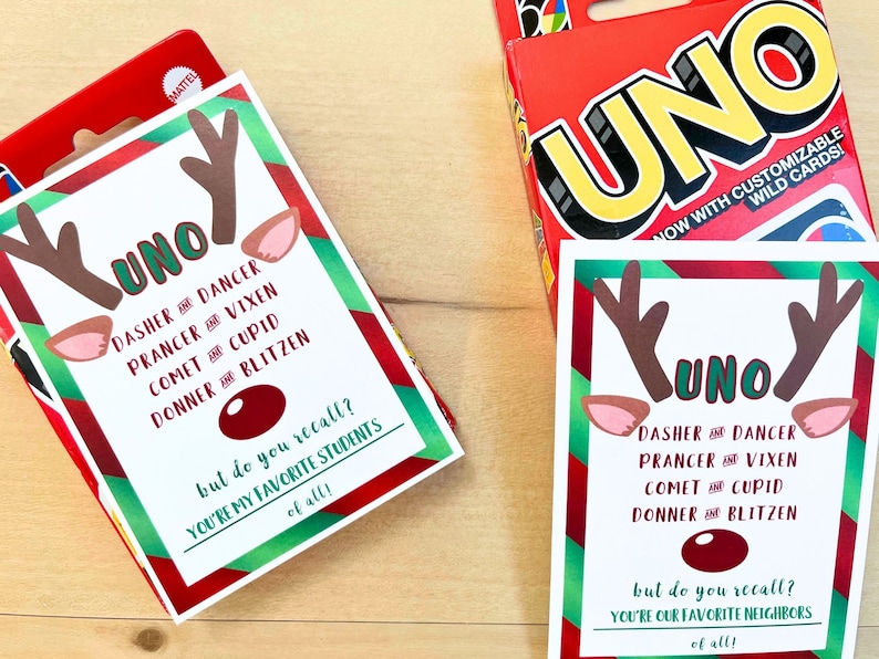 May include: Two UNO card game boxes and cards with a reindeer theme. The cards feature reindeer antlers, ears, and a red nose, with text that reads "UNO" and the names of Santa's reindeer. The box is red with the word "UNO" in large yellow letters.