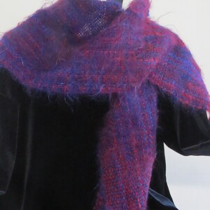 May include: A long, fuzzy scarf in shades of purple and red. The scarf is woven with a textured pattern and has long fringe at the ends.