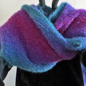 May include: A soft, fuzzy shawl in shades of blue, purple, and pink with fringe edges. The shawl is draped over a black garment.