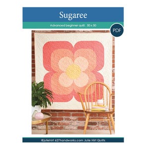 May include: A colorful quilt with a floral design, featuring shades of pink, orange, and yellow. The quilt is displayed against a brick wall, with a wooden chair and side table in the foreground. The text "Sugaree" and "Advanced beginner quilt. 50 x 50" are visible.