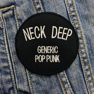 Op de afbeelding: Zwart-wit geborduurde patch met de tekst "Neck Deep" en "Generic Pop Punk" op een denim achtergrond.