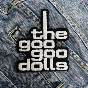 May include: Black and white embroidered patch with the text "the goo goo dolls" in a stylized font. The patch is on a blue denim background.