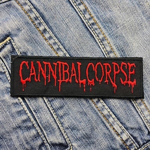 Op de afbeelding: Een rechthoekige zwarte patch met de rode geborduurde tekst "CANNIBAL CORPSE". De tekst heeft een druipend bloedeffect. De patch staat op een denim achtergrond.
