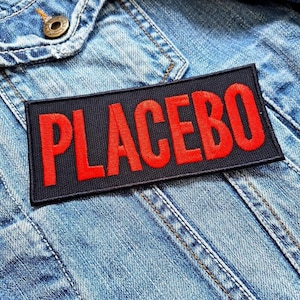 May include: A black patch with the word "PLACEBO" in red embroidered letters, sewn onto a blue denim jacket.