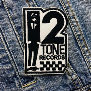 May include: Black and white iron-on patch featuring a silhouette of a person standing in front of a large number "2" with the text "TONE RECORDS" below. The patch has a checkered pattern at the bottom.