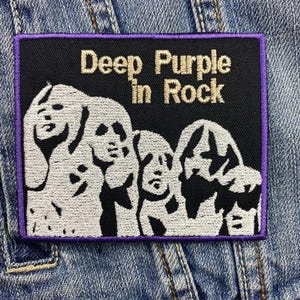 Könnte beinhalten: Ein gestickter Patch in Schwarzweiß mit einem violetten Rand. Der Patch zeigt eine Band aus vier Figuren mit dem Text "Deep Purple in Rock" darüber.