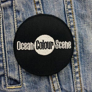 Op de afbeelding: Zwart-wit geborduurde patch met de tekst "Ocean Colour Scene" op een denim achtergrond.