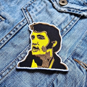May include: Yellow and brown embroidered patch of Elvis Presley's face on a denim background.