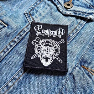 Peut inclure: Patch brodé noir et blanc avec le texte "Enslaved" et un crâne avec des épées et des haches.