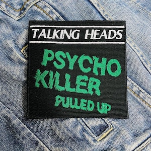 Könnte beinhalten: Ein schwarzer quadratischer Aufnäher mit dem weißen Schriftzug "TALKING HEADS" über "PSYCHO KILLER" und "PULLED UP" in Grün. Der Aufnäher befindet sich auf einer Jeansjacke.