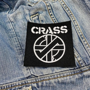 May include: Black and white embroidered patch with the word "CRASS" and a circle with a diagonal line through it.