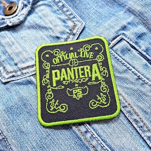 Könnte beinhalten: Ein quadratischer Aufnäher mit dem Text "OFFICIAL LIVE PANTERA" in Neongrün auf schwarzem Hintergrund. Der Aufnäher hat einen grünen Rand und ist auf eine Jeansjacke genäht.
