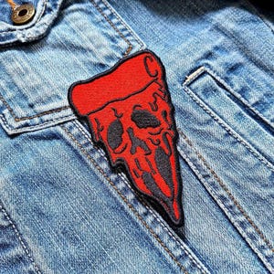 Könnte beinhalten: Roter und schwarzer gestickter Bügelaufkleber einer schmelzenden Pizzastückes mit Totenkopf-Design.