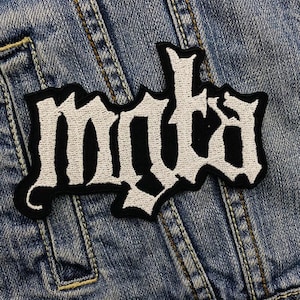 Pode incluir: Patch branco bordado "MYDA" em uma jaqueta jeans azul.
