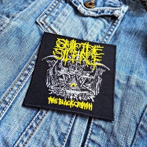 Może przedstawiać: Czarna i żółta naszywka haftowana z tekstem "Suicide Silence" i "The Black Crown" na czarnym tle.
