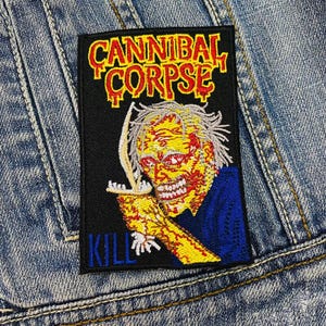 Puede incluir: Parche bordado en negro y amarillo con el texto "Cannibal Corpse" y "Kill" en rojo y blanco. El parche presenta un gráfico de un zombi sosteniendo un cuchillo.