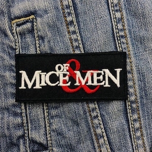 May include: Black and white embroidered patch with the text "Of Mice & Men" in white lettering with an ampersand in red.